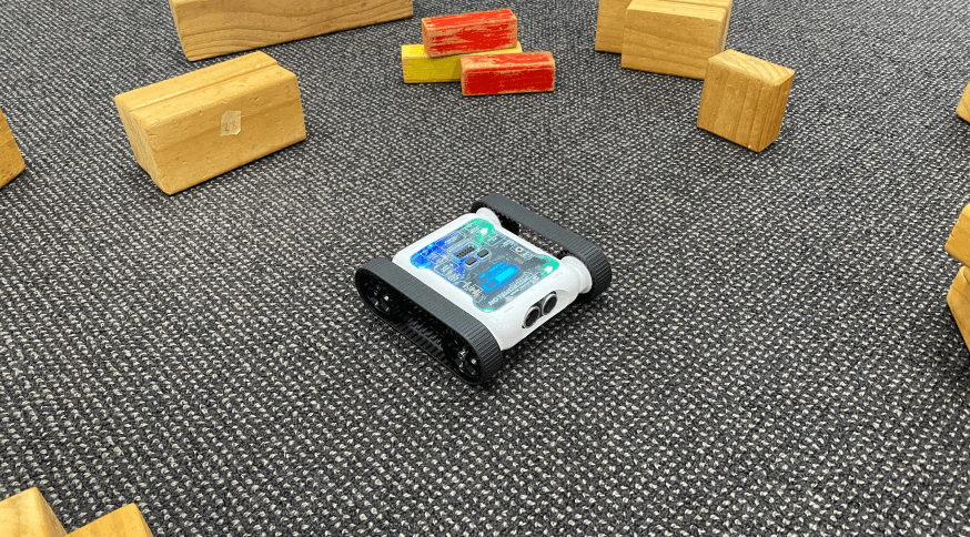 Micromelon Rover driving across classroom carpet between wooden blocks